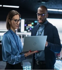 A man and a woman standing in front of a laptop, appearing to review information or work on a project together