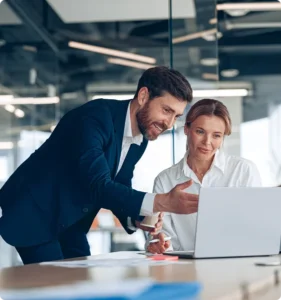 A man and woman collaborating while looking at a laptop screen together in a bright, modern workspace